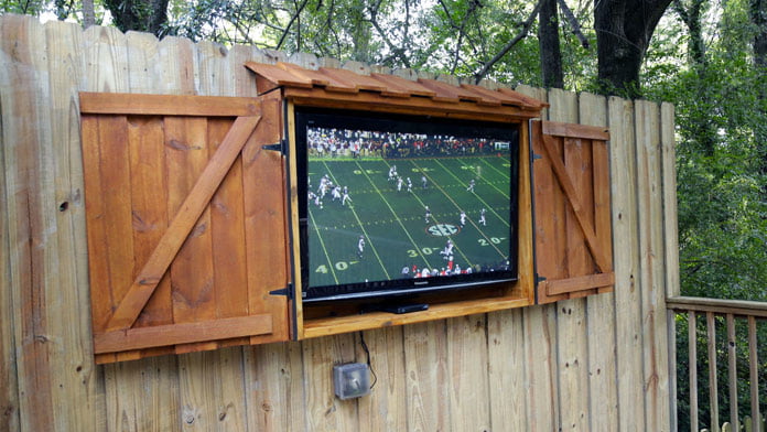 Juego de fútbol en un televisor de pantalla plana alojado en un mueble de televisión al aire libre hecho de madera